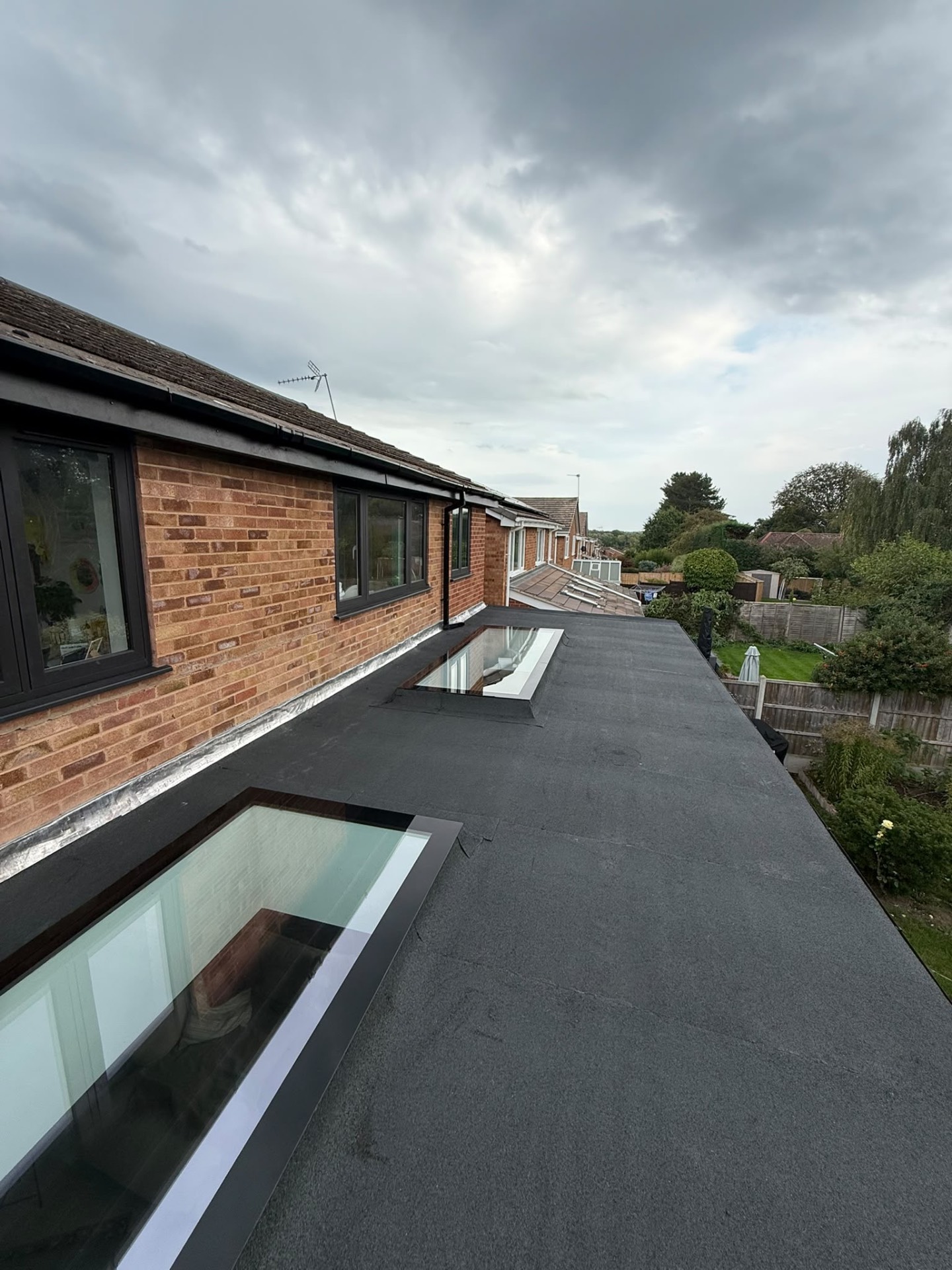 Two rooflights sealed into the new felt roof, with flashing running along the brick wall of the house