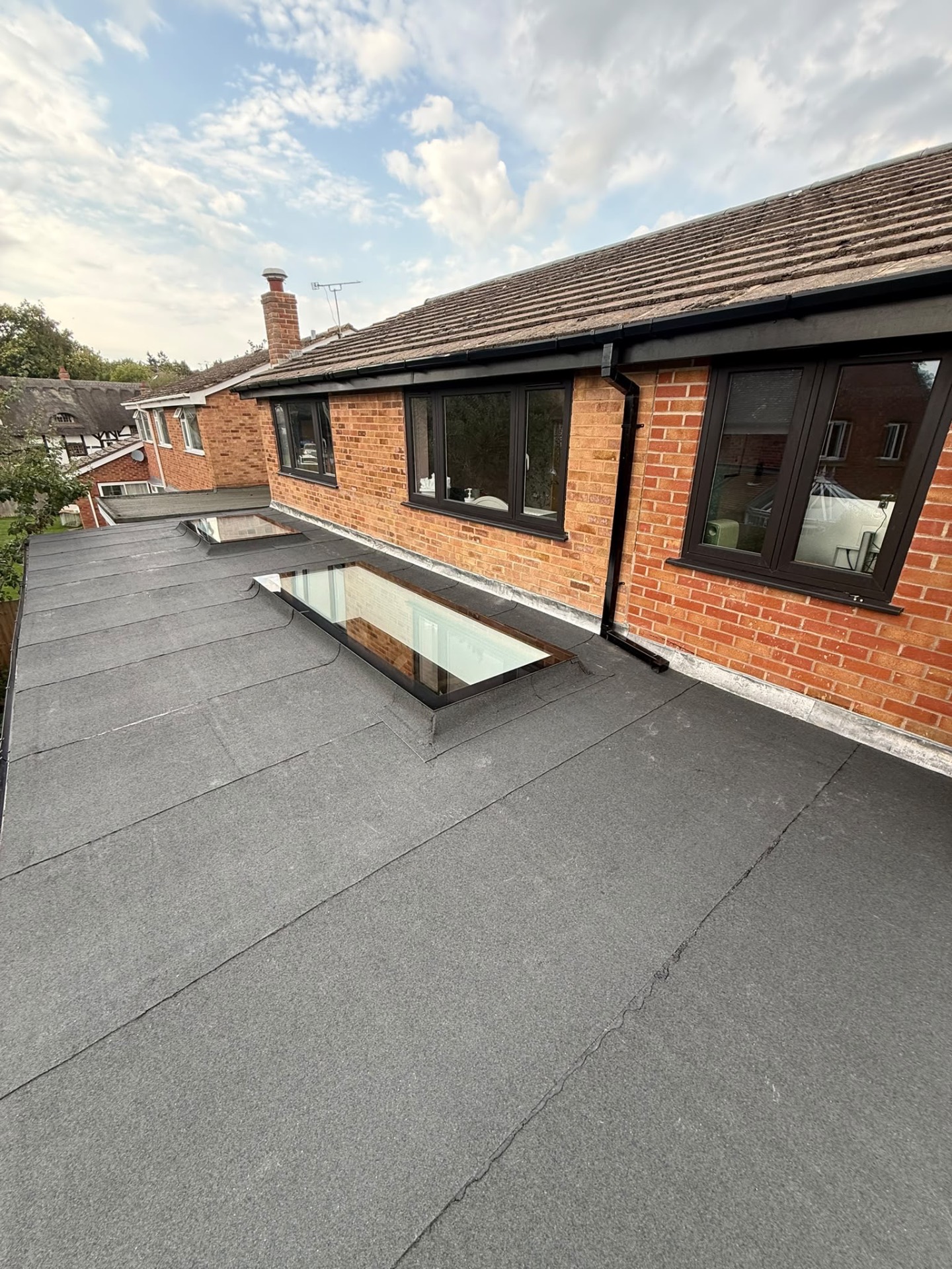 Completed flat roof with two rooflights set into new felt, next to the brick wall and windows of a Coventry house